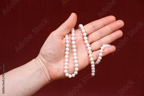 Young woman holding string of beautiful shiny small freshwater white pearl beads on red fabric background