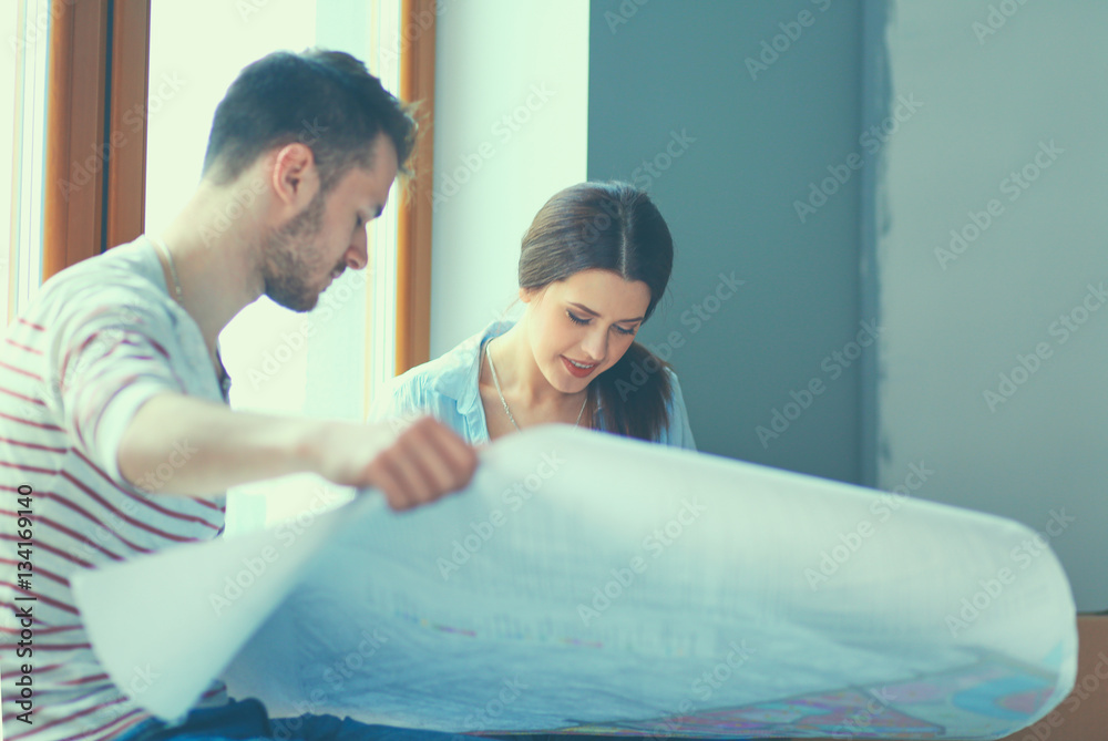 Obraz premium Young couple sitting on the floor and looking at the blueprint of new home