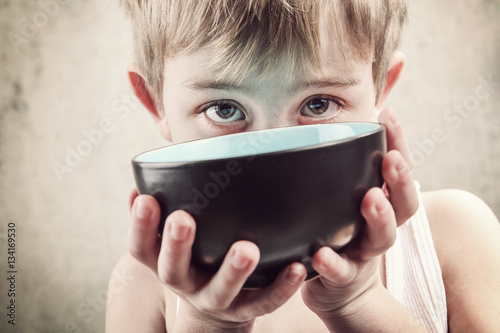 Toned image of a hungry child holding an empty bowl. photo