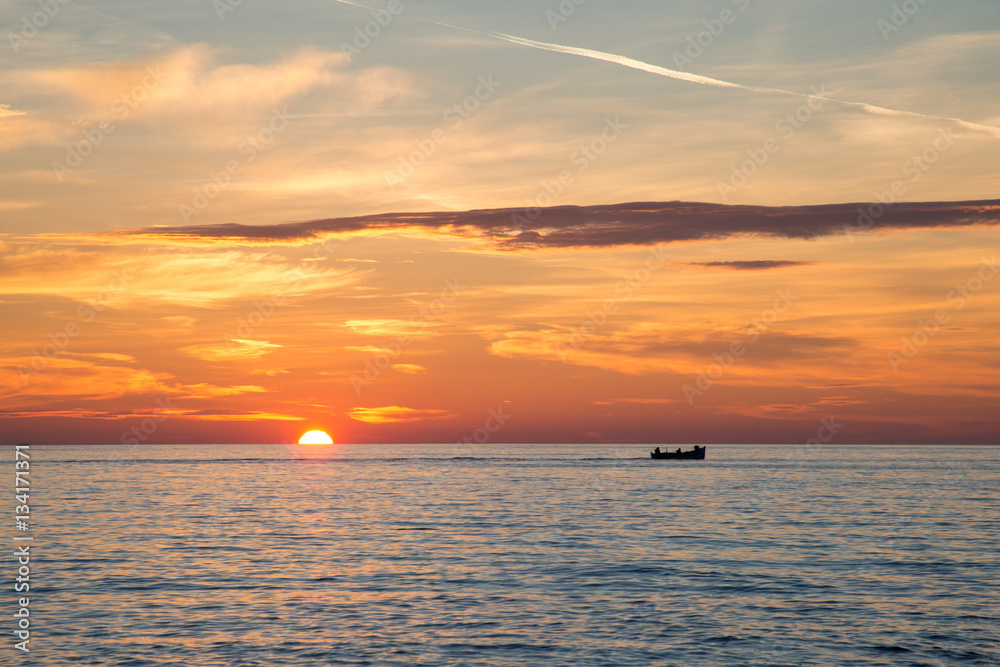 Fishing boat on the background of incredible golden sunrise, clouds and rising sun.