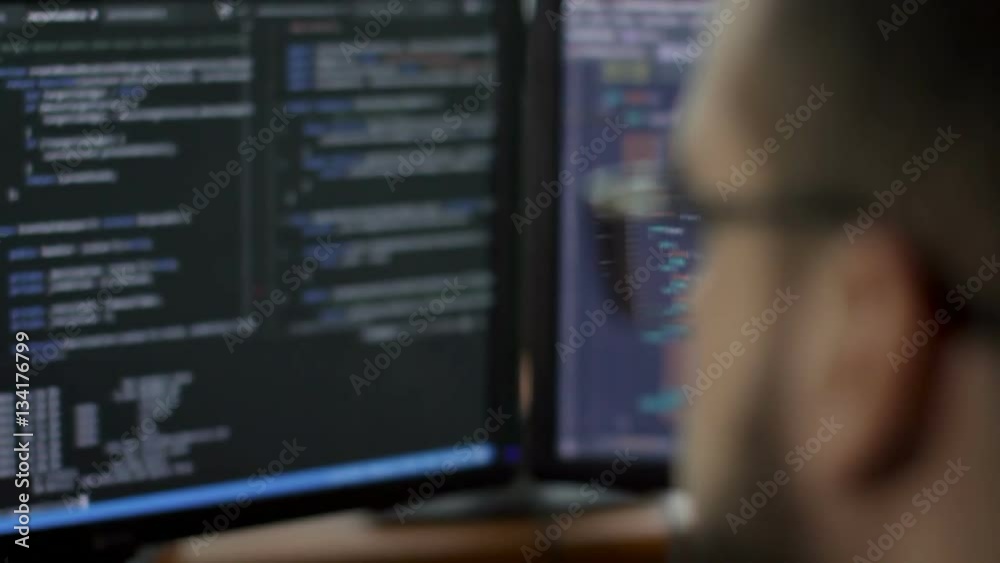 a young man with a beard and glasses works behind a computer