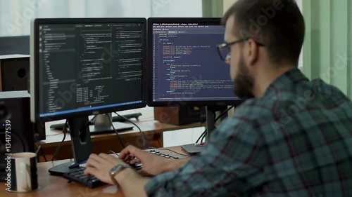 a young man with a beard and glasses works behind a computer