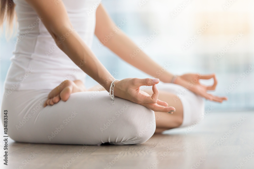 Young attractive yogi woman practicing yoga, sitting in Padmasana, exercise, Lotus pose with mudra, working out, wearing white sportswear, indoor, meditation session near window. Midsection close up - obrazy, fototapety, plakaty 
