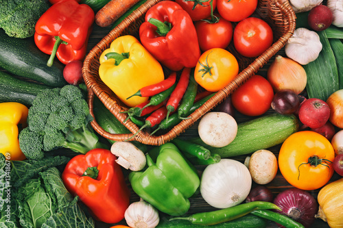 Wicker basket with fresh vegetables on background