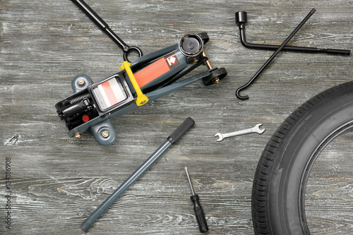 Car jack with tools and tire on wooden background