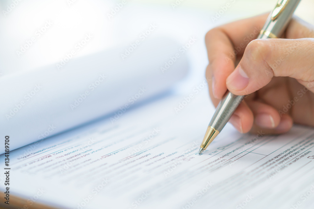 Hand with pen over application form . Hand with pen over application form .