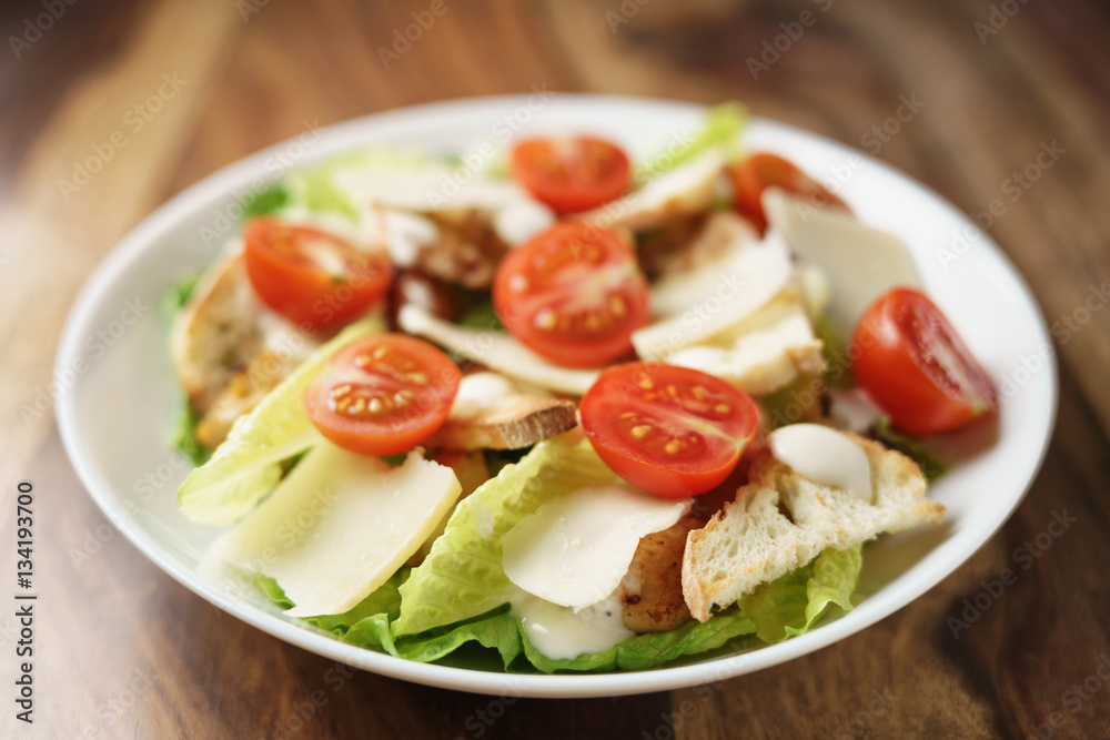 fresh homemade caesar salad with chicken and cherry tomatoes on wood table, shallow depth of field