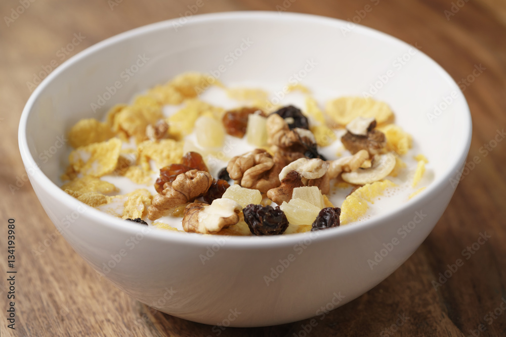 closeup photo of corn flakes with fruits and nuts in white bowl on wood table, simple healthy breakfast closeup photo of corn flakes with fruits and nuts in white bowl on wood table, simple healthy breakfast