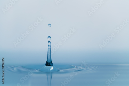 clear blue water drop with ripple on surface, shot from side with shallow focus