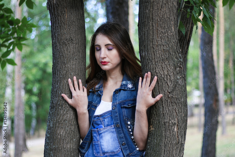 Woman in overalls stands between tree trunks Woman in overalls stands between tree trunks