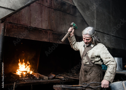 Foto Gray-haired smith forges detail in the smithy