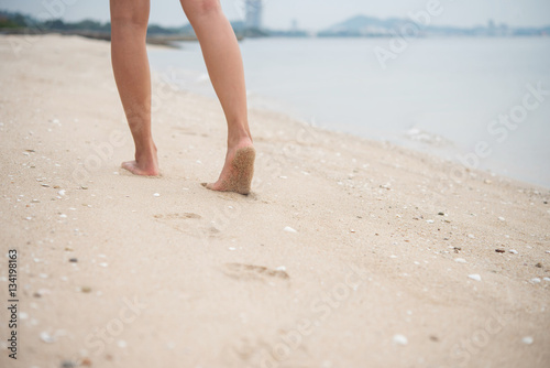 Young woman walking on sand beach leaving footprints in the sand