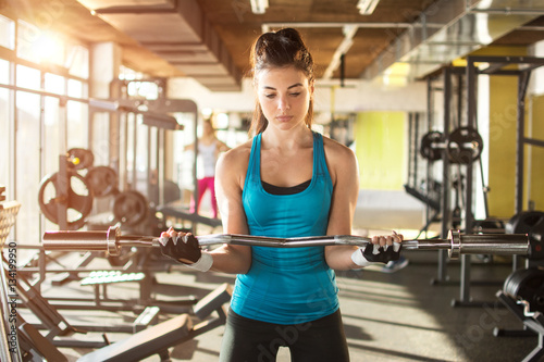 Young fit woman working out with curl bar in gym.