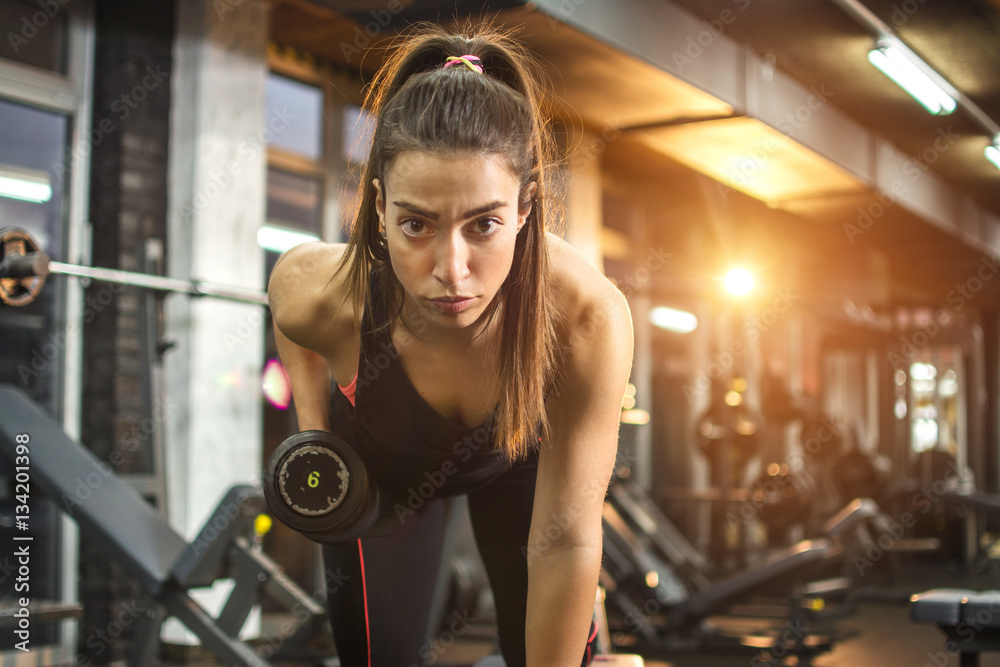 Athletic woman pumping up muscles with dumbbells in gym. Athletic woman pumping up muscles with dumbbells in gym.