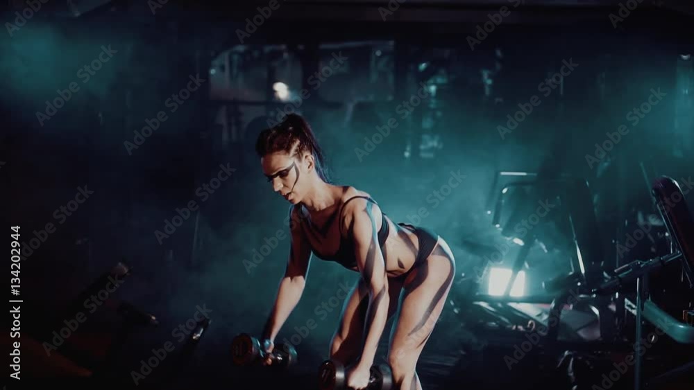 Torso of a young fit woman lifting dumbbells on dark background Torso of a young fit woman lifting dumbbells on dark background