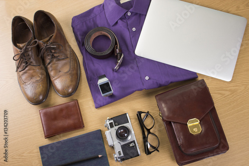 Business Mans setup. Shoes, camera, laptop, wallet, notebook, shirt on a wooden table.