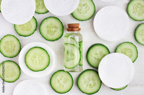  Fresh homemade vegan facial toner in bottle, green cucumber slices, cotton-pads, top view ingredients.