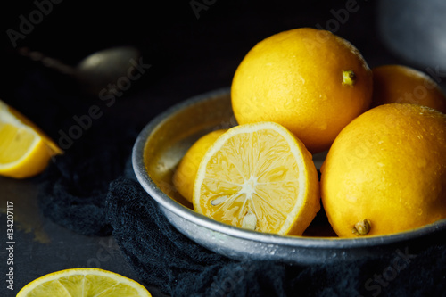 Beautiful ripe lemons in plate on a black background © mikhail_kayl