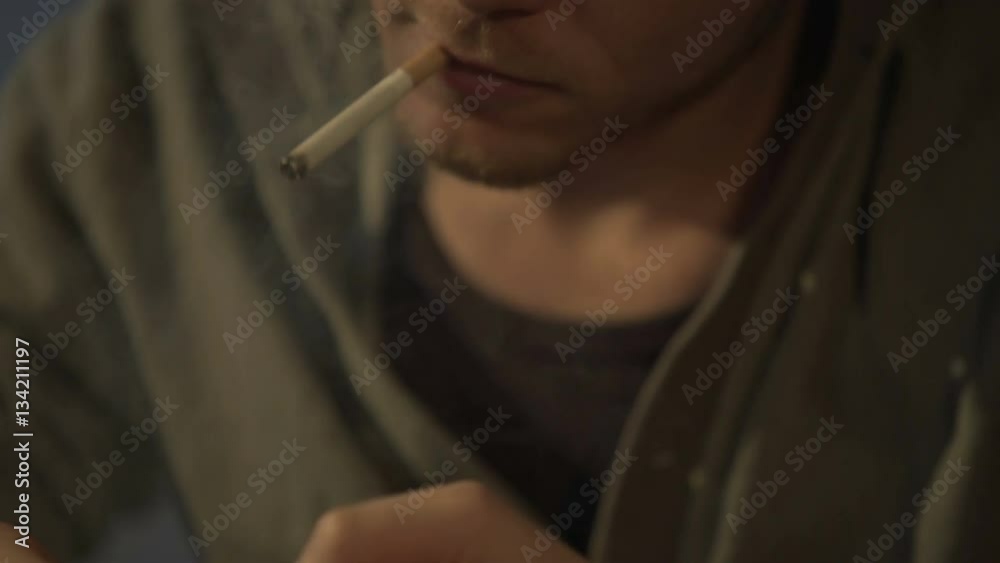 Young man lighting cigarette, drug and gaming addict playing on smartphone