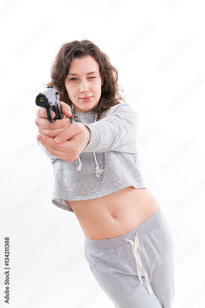 Young girl in a tracksuit with a gun. Beautiful young woman is aiming a revolver Young girl in a tracksuit with a gun. Beautiful young woman is aiming a revolver