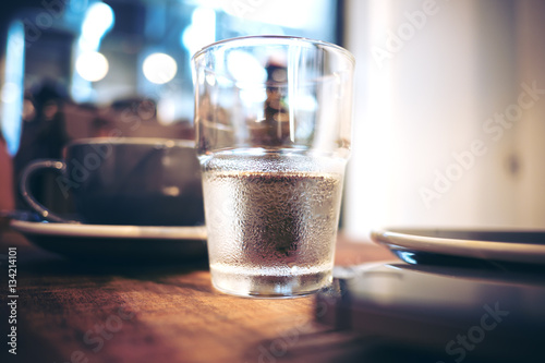 Water in clear glass and coffee cup on wooden table in cafe with blur background