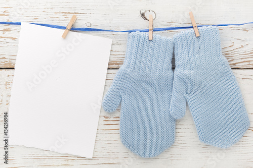 Small baby gloves, blank card on white wooden background. Flat lay. Top view