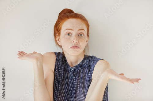 Puzzled and clueless young redhead woman with arms out, shrugging her shoulders, saying: who cares, so what, I don't know. Negative human emotions, facial expressions, life perception and attitude photo