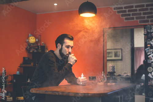 man smoking or vaping e-cig or electronic cigarette holding a mod with a lot of clouds