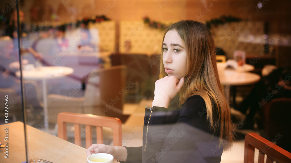 woman behind window in cafe. young girl in black dress sits at table, holding beverage cup woman behind window in cafe. young girl in black dress sits at table, holding beverage cup
