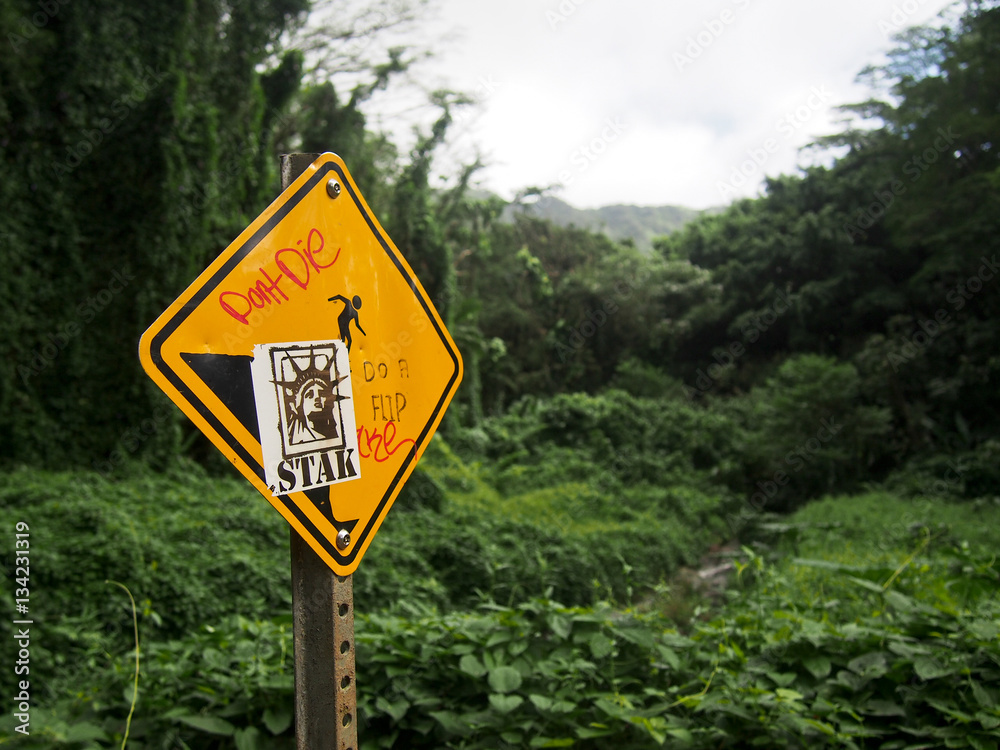 Warning sign on a hiking trail in Hawaii with grafitti warning hikers not to die