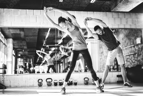 Black and white photo of attractive athletes stretching at the gym.
