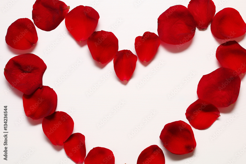 Heart of red rose petals on a white wooden background.
