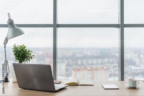 Workplace with notebook laptop Comfortable work table in office windows and city view.