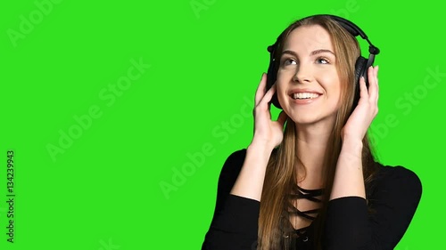 Closeup of beautiful woman with headphones listening to the music and blowing a kiss on green chroma key background
