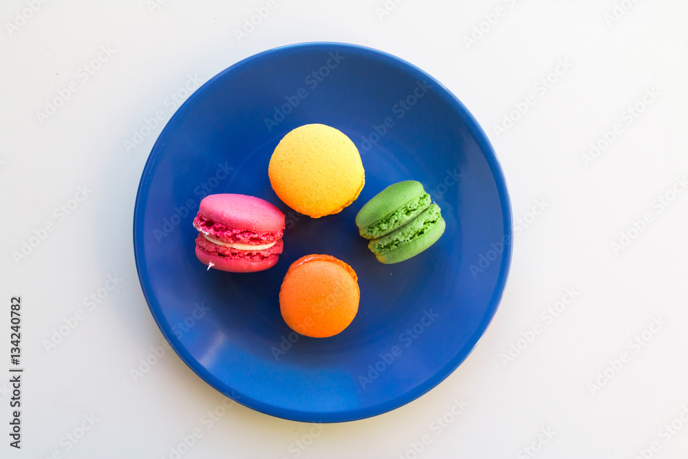 Yellow, orange, pink and green macaroons on blue round plate. Yellow, orange, pink and green macaroons on blue round plate.
