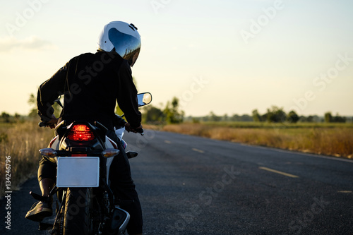 a man on the motorcycle parking on the road left side and sunset, to looking behind.