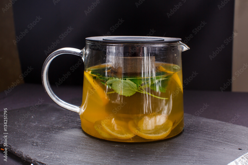 hot tea with mint and lemon in a glass pot on black background hot tea with mint and lemon in a glass pot on black background