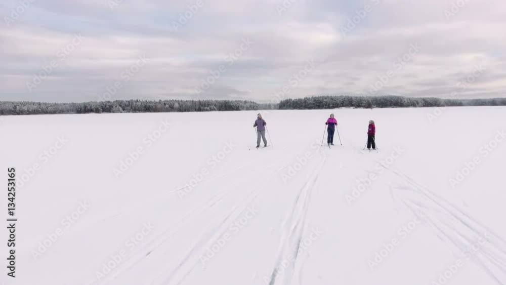 Caucasian family running on skies on the ice of lake at winter, suunset lights on sky at evening Caucasian family running on skies on the ice of lake at winter, suunset lights on sky at evening