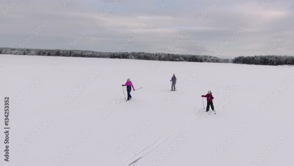 Camera flying around three sporty different ages female skiers running on cross-country ski. Frozen lake. Russia Camera flying around three sporty different ages female skiers running on cross-country ski. Frozen lake. Russia