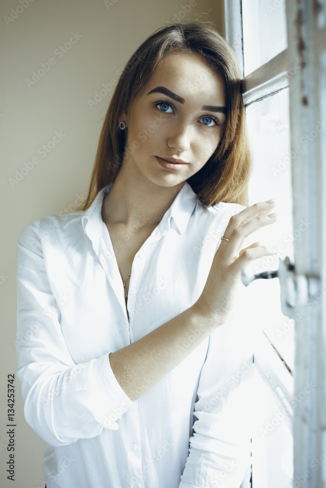 Smiling young brunette woman standing at the window