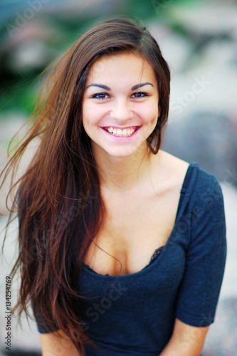 Portrait of a smiling beautiful long-haired brunette woman in a black t-shirt with a deep neckline with a blur effect in the background, closeup