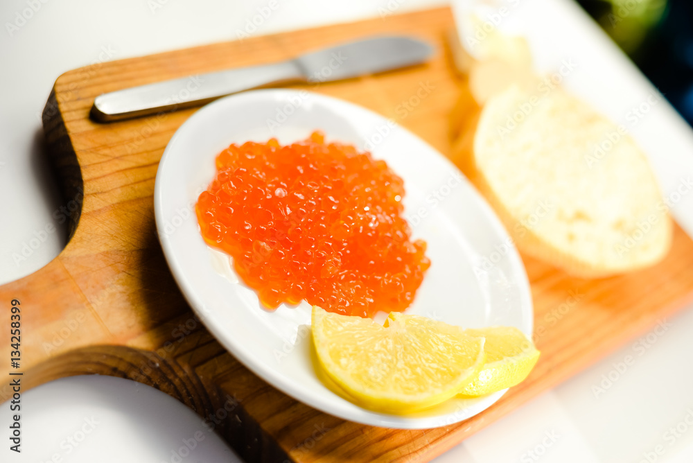 Red caviar, lemon and bread on wooden board white table background Red caviar, lemon and bread on wooden board white table background