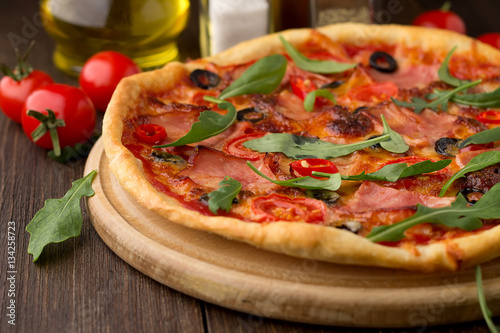 Italian traditional fast food: pizza with ham, tomatoes, olives, arugula.
