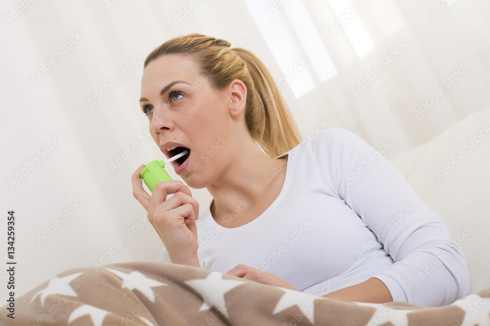 Young woman with sore using throat spray while lying in bed Young woman with sore using throat spray while lying in bed