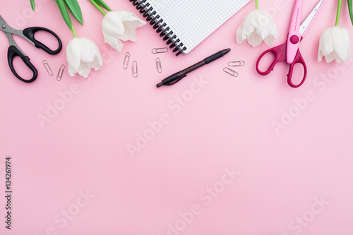 Flat lay, top view office table desk. feminine desk workspace with notebook, pen, scissors, floral bouquet on pink background.