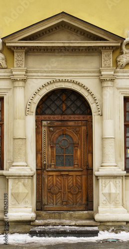 Antique classic pastel marble facade with rough rustic sculptured wooden door and old monochrome stained glass. Vertical toned image.