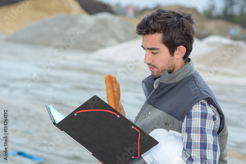 Man on construction site holding file and baguette