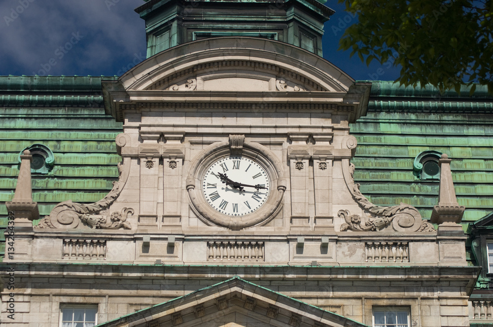 Clock of City Hall in Old Montreal, Quebec, Canada.  Mansard roof, fleur de lis, and rounded pediment architectural details of New French Imperialism architecture.