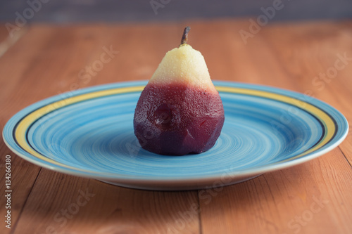 one poached pear on blue big dish plate on wooden background