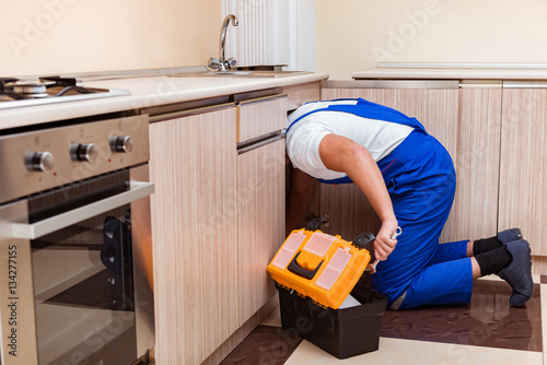 Young repairman working at the kitchen